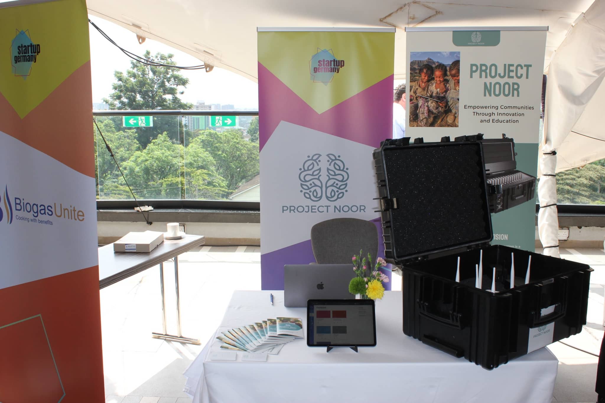 Der Messestand von Project Noor: Roll-ups, der geöffnete Transportkoffer mit Ladefächern und ein Tablet mit der Lernplattform auf dem Tisch.
